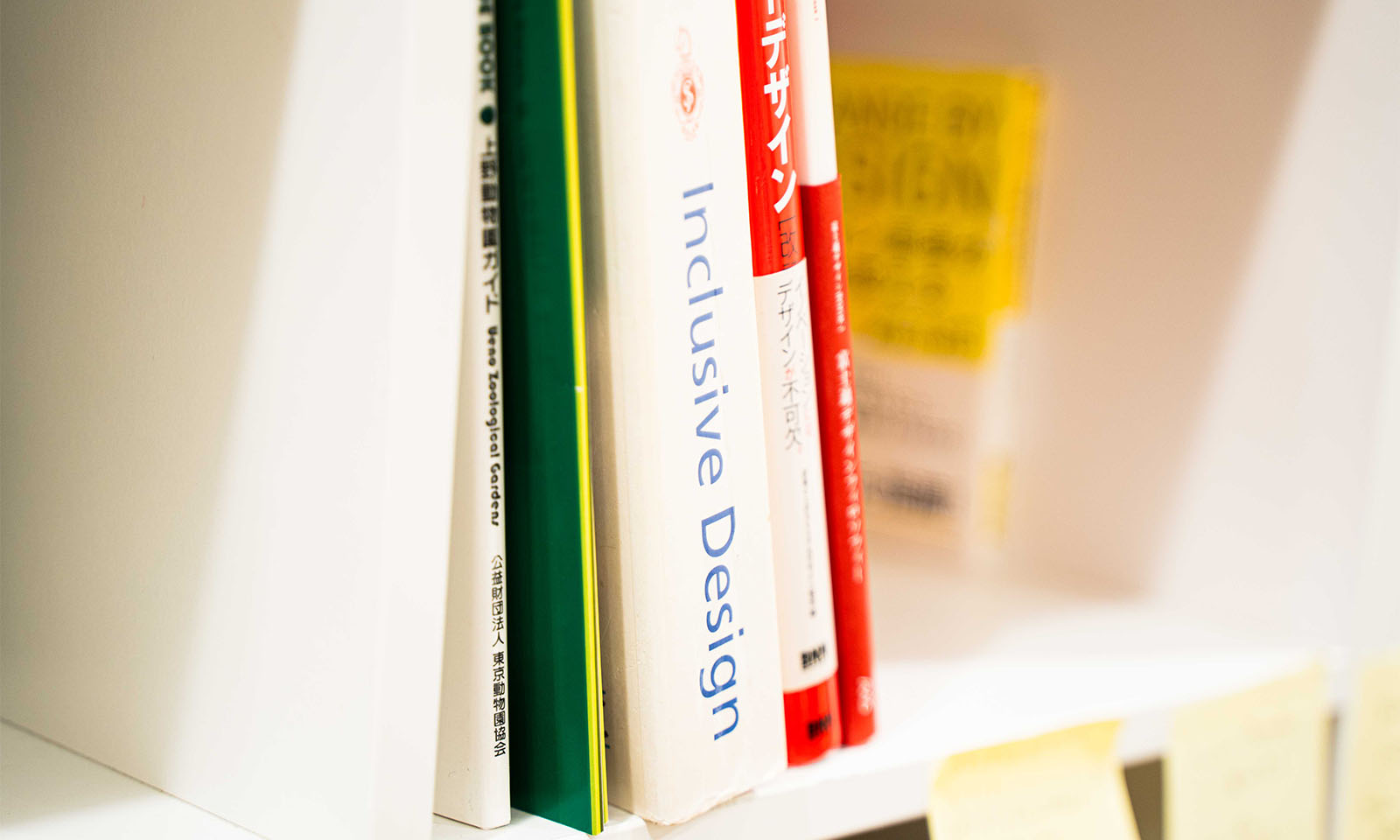 ALTはじまり。平井教授の研究室におかれた本棚の中。「インクルーシブデザイン」と英語で書かれた昔の電話帳くらいの厚みのある本が置かれている。ALTおわり。