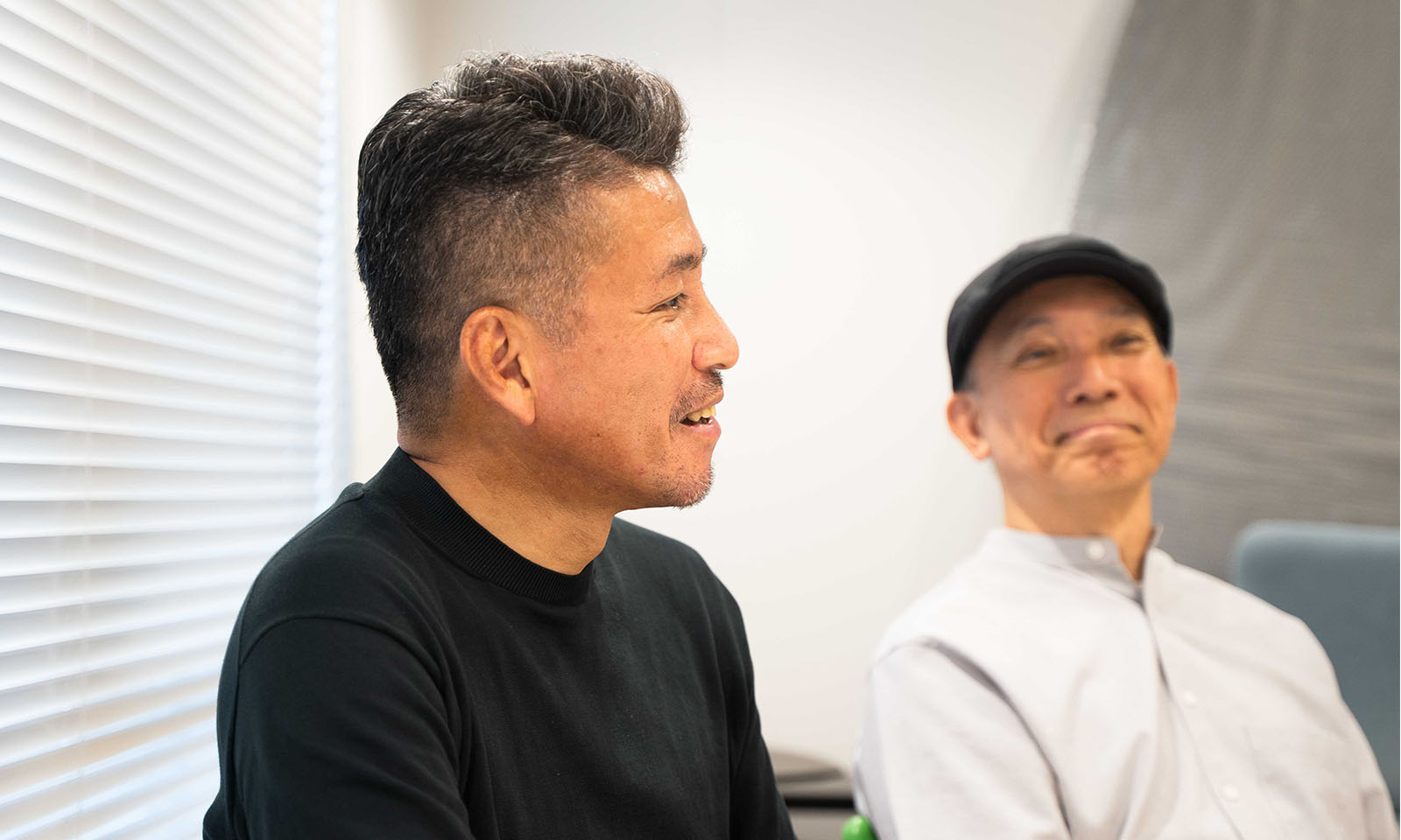 ALTはじまり。少しグレイッシュの髪色で整えられた短髪に、黒のTシャツを着るコクヨの太田さん。柔らかな表情で話す様子。その背後には太田さんが語られるのをやさしく微笑む平井先生。ALTおわり。