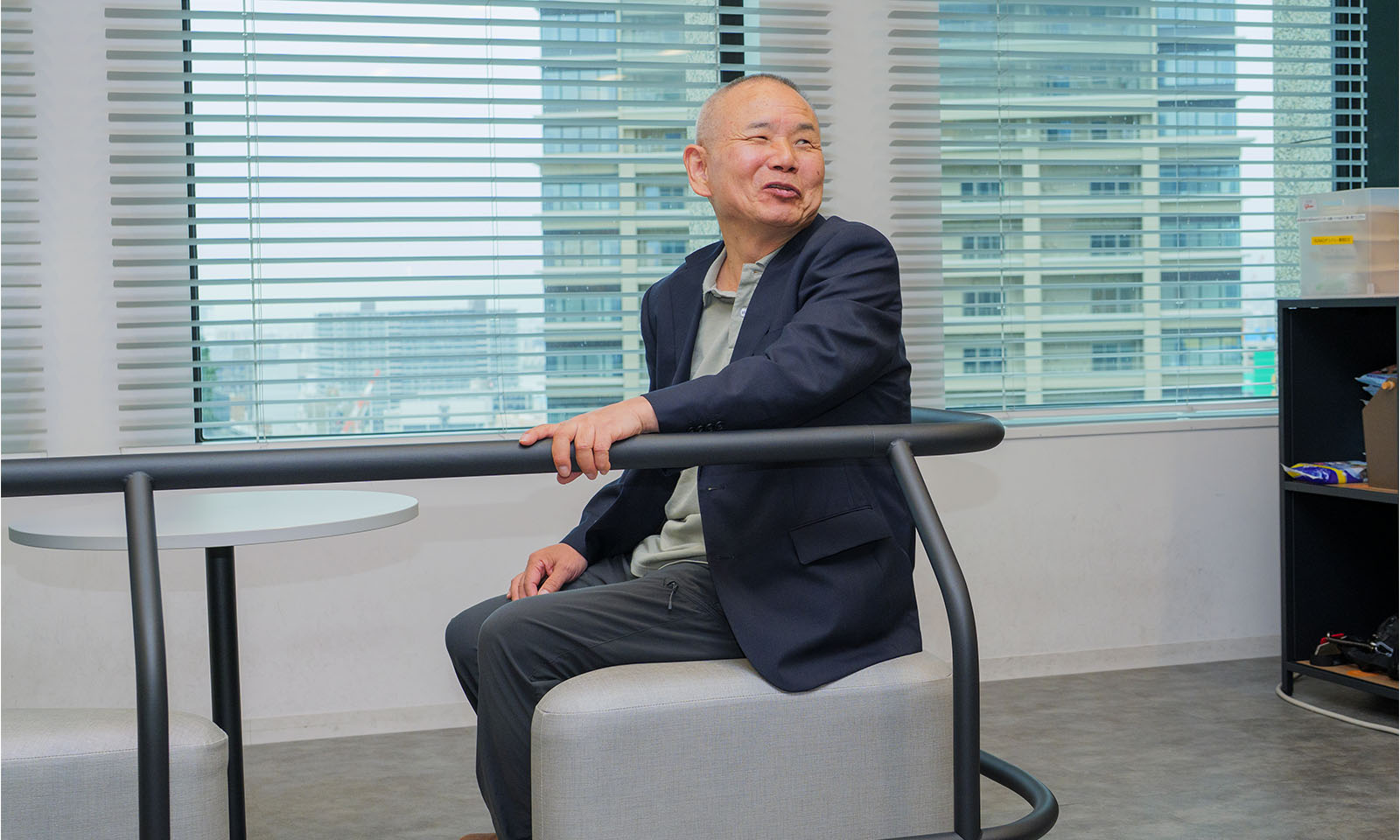 ALTはじまり。ブルーのジャケットと黒のパンツ姿でHangoutのソファに座り、手すりに肘をかけている笑顔の宮原さん。ALTおわり。