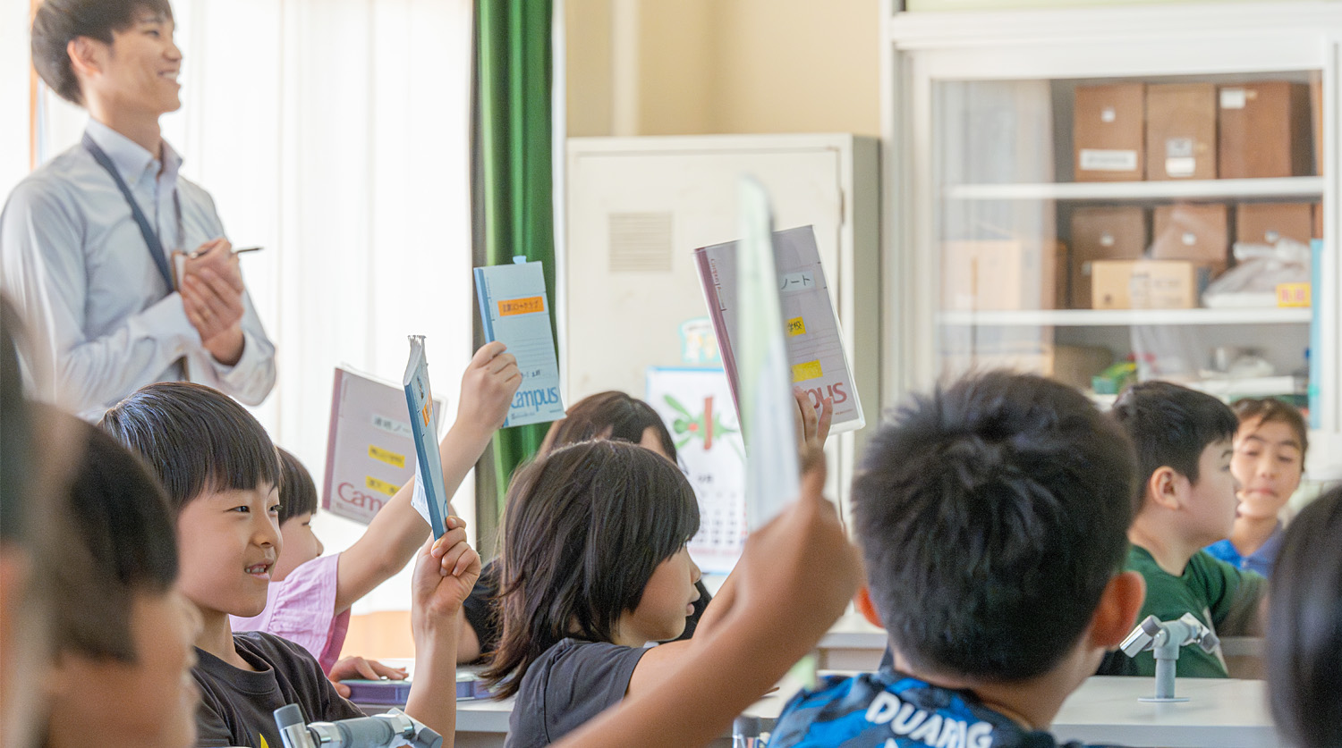 小学校での授業の様子。子供達が笑顔でノートを掲げて見せてくれている。