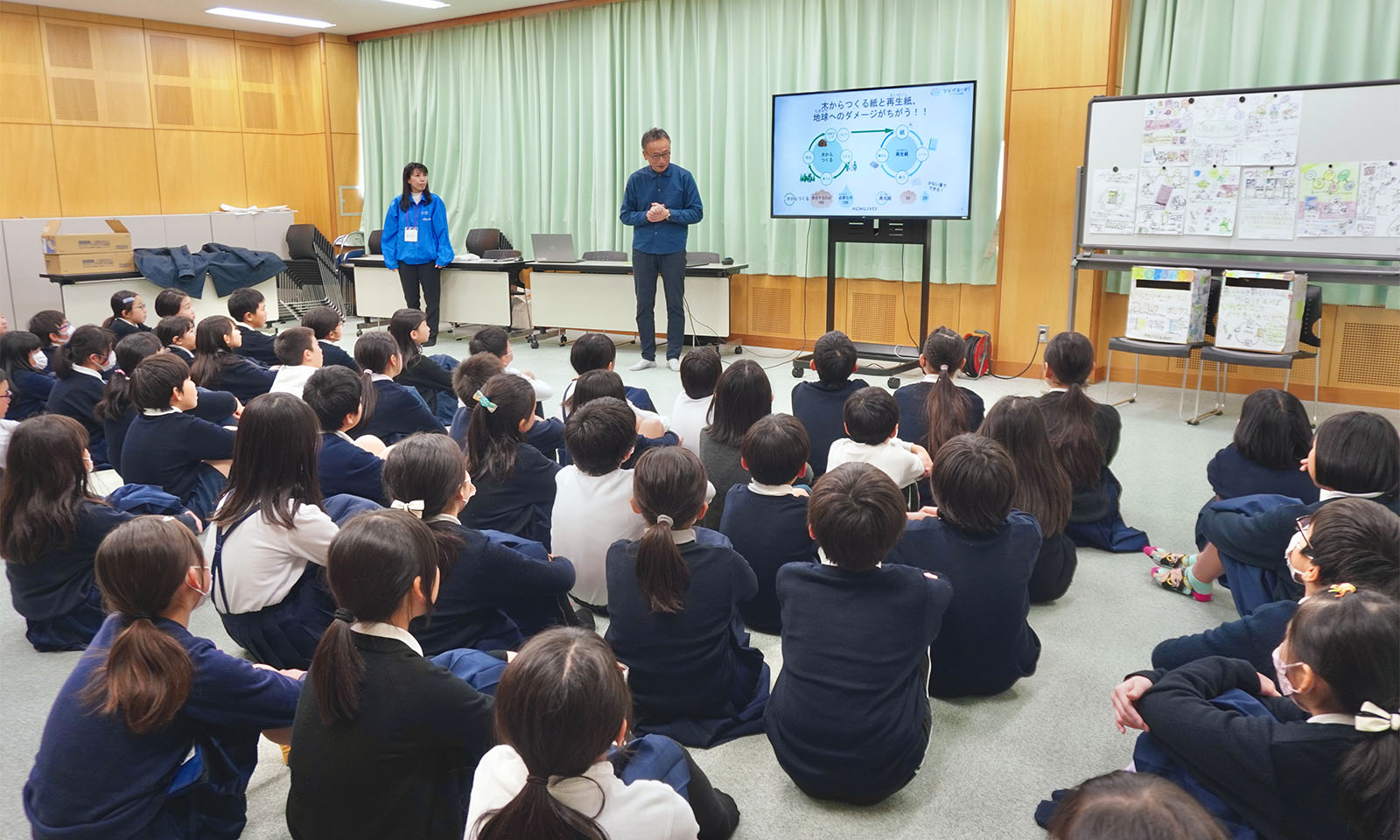 つなげるーぱ!の贈呈式の会場全体の画像、子供たちが前を向き体育座りをしている