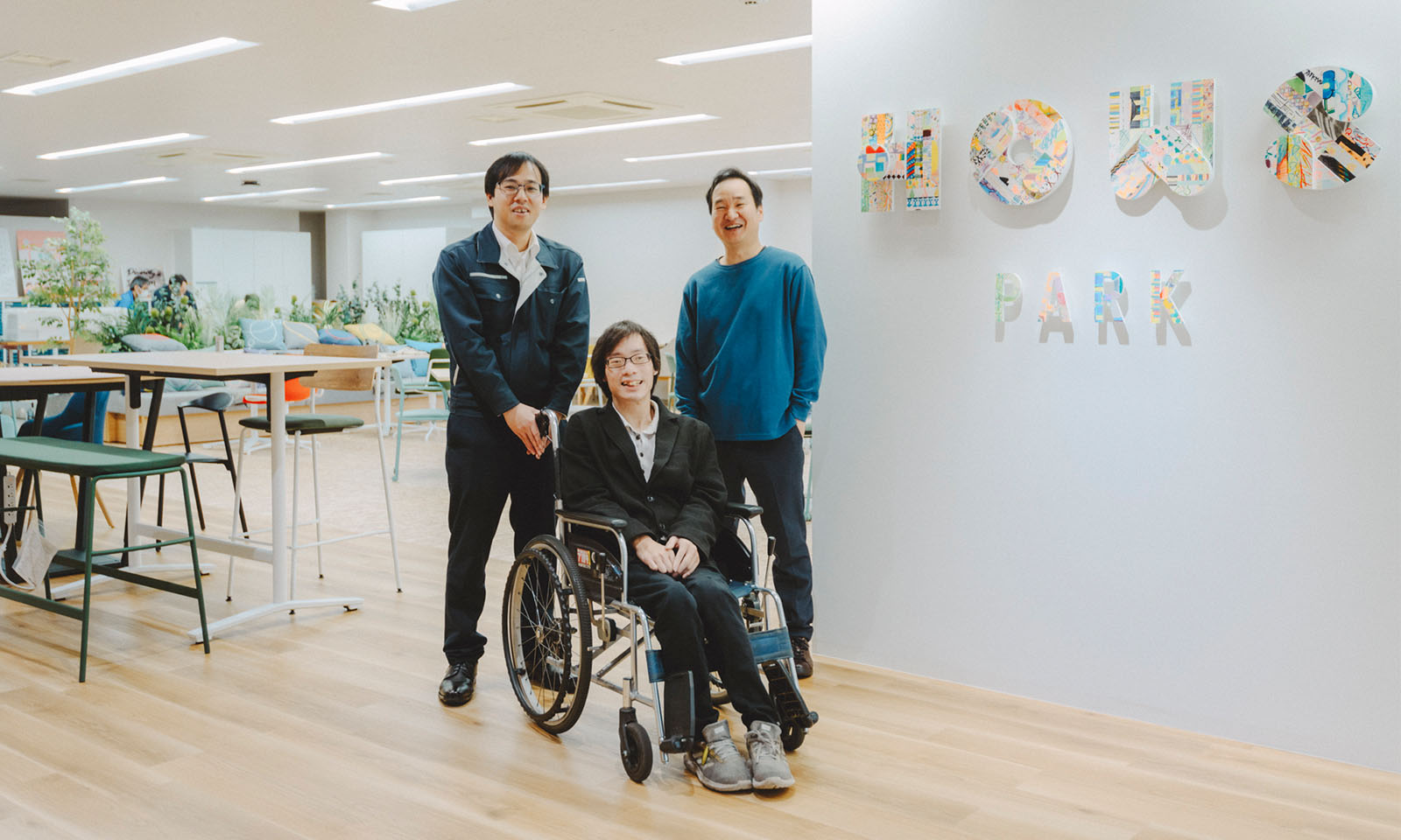 HOWS PARKの入り口の前でインタビューを受けた西林さんと車いすの近藤さんと平畑(ひらはた)さんが笑顔でカメラを見ている様子