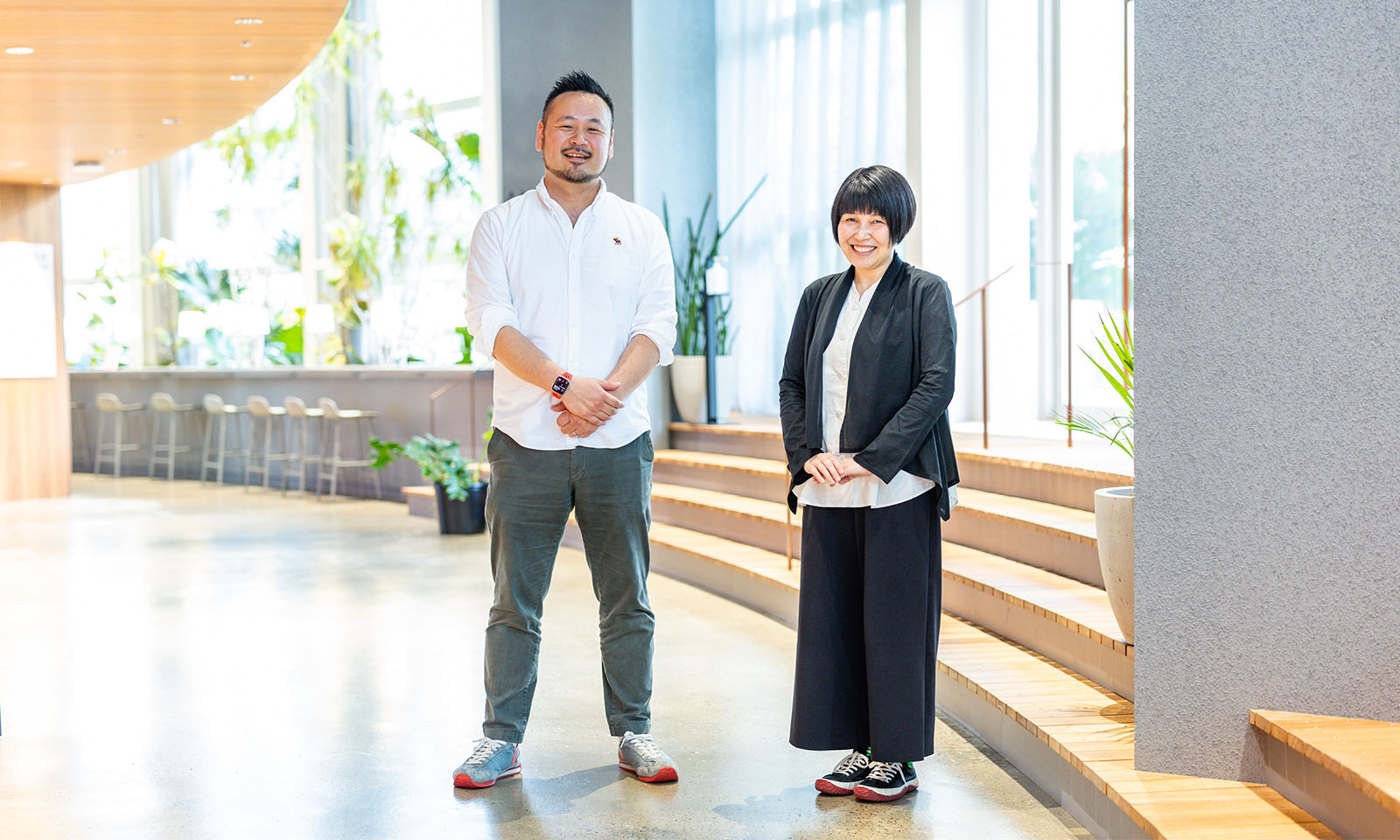 大きな窓のある明るい室内区間で、武田さんと、栗木さんが並んで立っている
