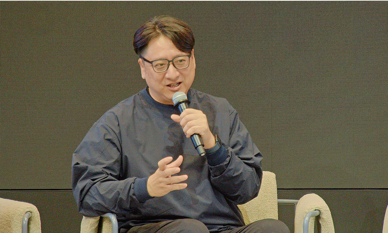 ALTはじまり。座談会のなかで発言をするコクヨ社長の英邦さん。右手にはマイクをもち、身振り手振りを交えながら話している。ALTおわり