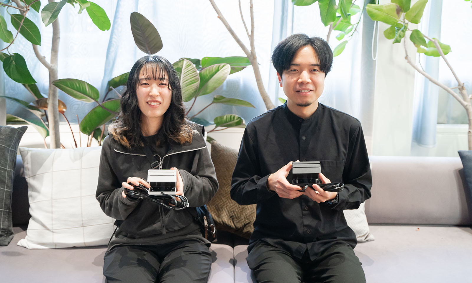 ALTはじまり。観葉植物が後におかれた薄いグレーのソファーに座る2人。ふたりとも優しい笑顔でカメラを見つめる。手元にはそれぞれ白と黒のエナジーラインをもち、その佇まいから思いを込めて作ったのだと伝わる。ALTおわり。